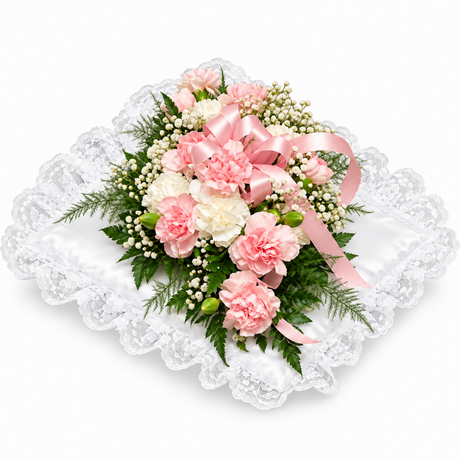Pink and white carnations, baby's breath, and green foliage with a pink satin ribbon on a white lace pillow.