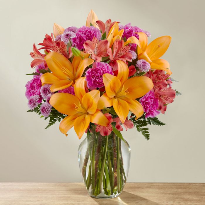 Orange lilies and hot pink mini carns in a glass vase Exquisite